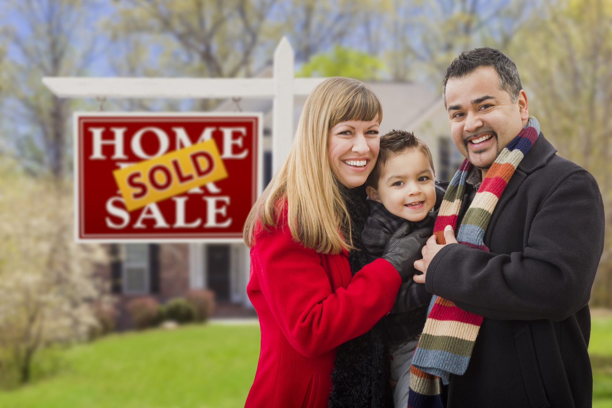 A Family Stands in Front of a “Home Sold” Sign.