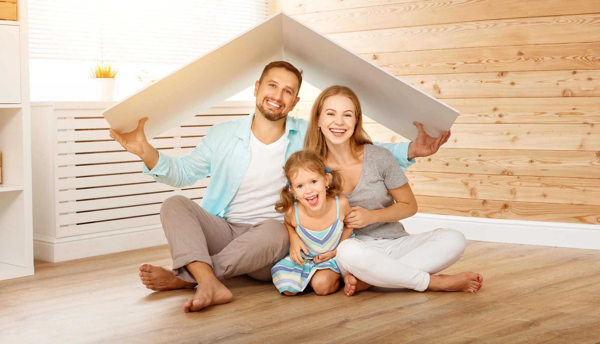 A Family Sitting on a Wooden Floor Under a Makeshift Tent Made of a Large Sheet of Paper.